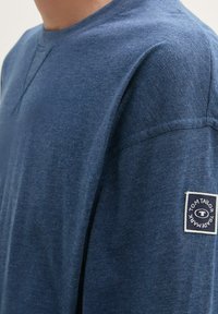 Blauwe katoenen T-shirt met een ronde hals, korte mouwen en een patchlogo op de linker mouw. Zachte textuur en casual pasvorm.