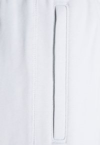 Světle modrá tkanina s hladkou texturou, obsahující vertikální kapsu a kontrastní stehy podél švů.