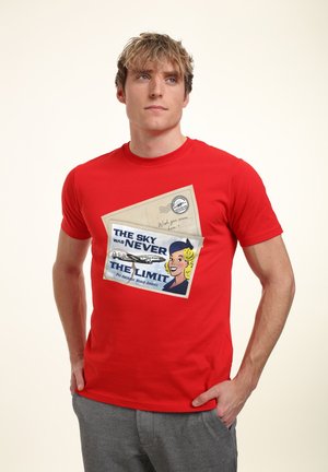 Rotes Baumwoll-T-Shirt mit einem grafischen Druck einer Retro-Postkarte, die Text, ein Flugzeug und eine Frau mit blonden Haaren zeigt. Kurzärmlig, Rundhalsausschnitt.