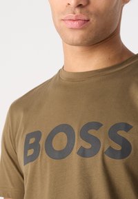 Alkūninis žalias medvilninis marškinėliai su apvalia iškirpte ir ryškiu juodu "BOSS" užrašu ant krūtinės. Minkšta tekstūra, neformalus dizainas.