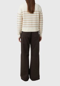 Kremowy sweter w brązowe paski, z prążkowanym dołem i mankietami, połączony z luźnymi, ciemnobrązowymi spodniami z tylnymi kieszeniami.