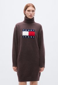 Καφέ πλεκτό φόρε�μα με ψηλό ζιβάγκο, μανίκια με ριμπ ύφανση και κεντρικό λογότυπο σε μπλε ναυτικό, κόκκινο και άσπρο. Υφή υφάσματος με ανάγλυφο φινίρισμα.