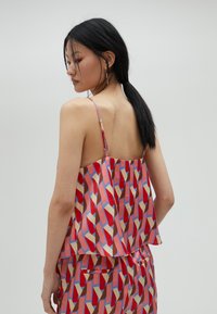 Šarena bezrukavna majica u crvenoj, plavoj i bež geometrijskoj šari. Glatka tkanina s opuštenim krojem i podesivim trakama.