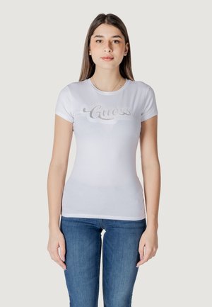 T-shirt blanc ajusté à manches courtes, arborant un logo "Guess" en strass argenté sur la poitrine. Matière en coton doux.