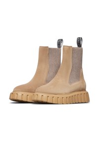 Botas de tobillo de ante beige con paneles laterales elásticos, suelas de goma texturizada y tiradores negros. Presenta un diseño de suela gruesa y estriada.