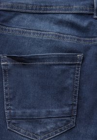 Vaqueros de denim azul oscuro con un único bolsillo trasero y costuras en contraste. La tela tiene una textura suave y un ligero desgaste.