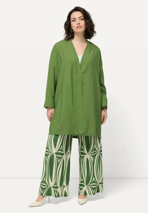 Camicia giacca verde a maniche lunghe con scollatura a V, abbinata a pantaloni larghi con un motivo geometrico verde e crema.
