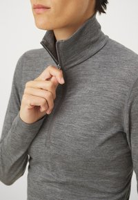 Šedý pulóver na zips vyrobený z textúrovanej tkaniny, ktorý má vysoký golier a polovičné zapínanie na zips, zdôrazňujúci priliehavý strih.