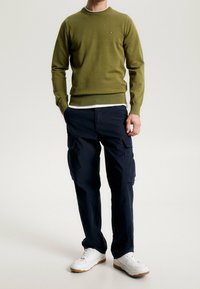 Pull en maille vert olive à col rond, associé à un pantalon cargo bleu marine foncé avec poches latérales. Baskets blanches avec semelles texturées.