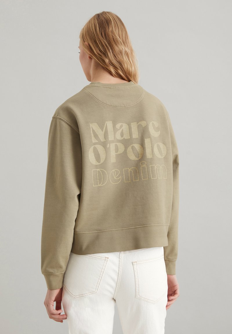 Olivenfarbener Sweatshirt mit lockerer Passform, auf der Rückseite mit einem großen cremefarbenen Logo-Print versehen. Der Stoff wirkt weich und hat gerippte Bündchen.