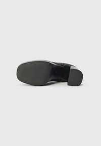 Zapato de tacón alto negro con parte superior de piel suave y suela de goma texturizada. El tacón tiene forma de bloque y mide aproximadamente 7,5 centímetros.