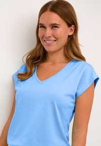 T-shirt bleu clair en V fabriqué à partir d'un tissu lisse, avec des manches courtes retroussées et une coupe décontractée. Pas de motifs ni de matériel visible.