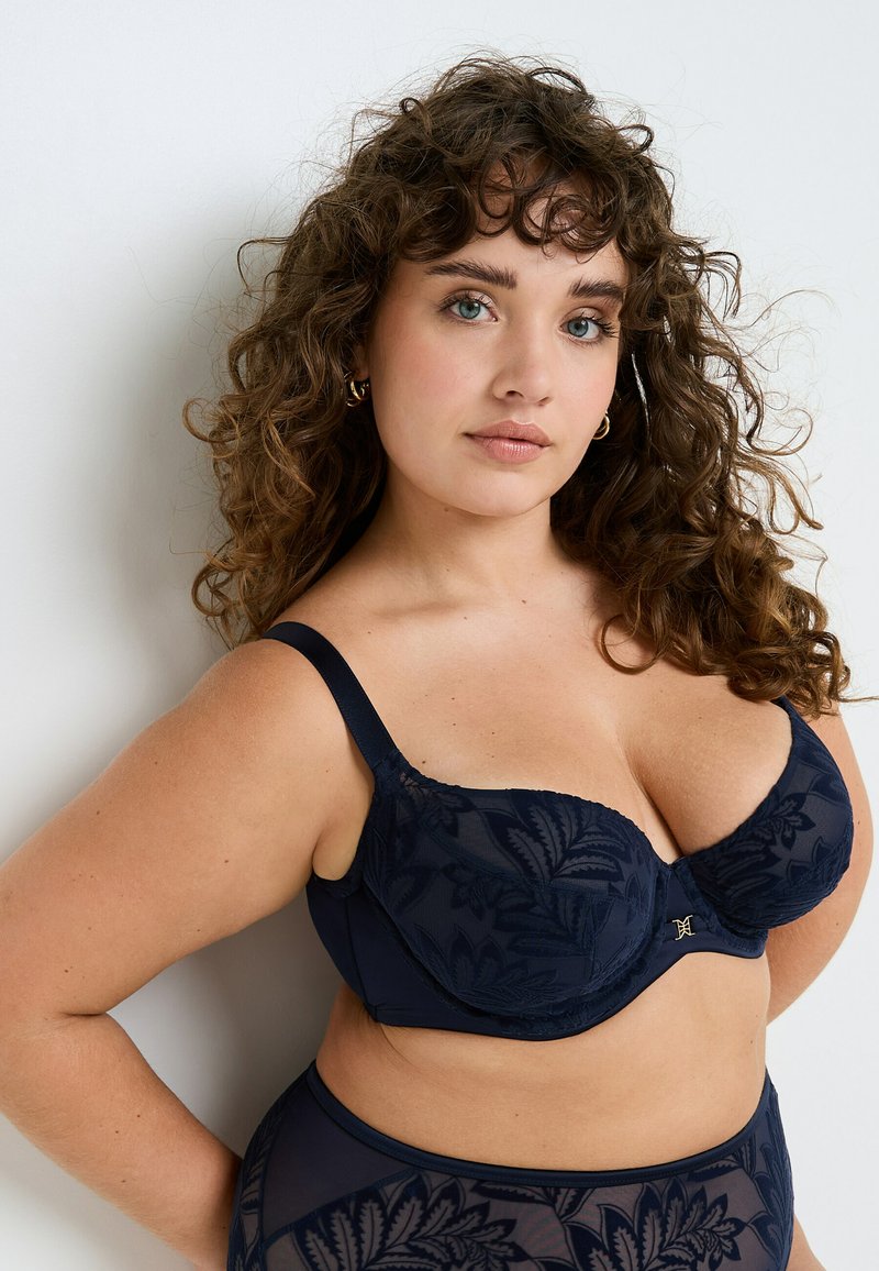 Reggiseno blu navy con motivo floreale, dotato di supporto con ferretto, spalline regolabili e dettagli in pizzo testurizzato. Finish liscio alle coppe.