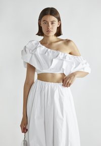 Hvid crop top med volang design uden skuldre og en hvid højtaljet nederdel med samlet stof og elastisk talje.