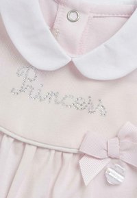 Robe rose clair avec un col blanc, ornée de "Princess" en sequins argentés et d'un ruban rose clair avec un accent en plastique.