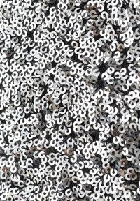 Czarna tkanina pokryta nachodzącymi na siebie srebrnymi i białymi cekinami w spiralnym wzorze, odbijającymi światło i tworzącymi teksturowany wygląd.