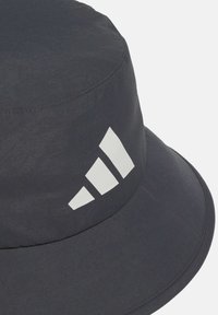 Sort bøttehat med en bred, rund skygge og en glat tekstur. Har et fremtrædende hvidt tre-stribe logo på den ene side.