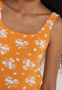 Débardeur orange avec motif floral blanc, doté d'un décolleté carré et de larges bretelles. Fabriqué en tissu doux et respirant.