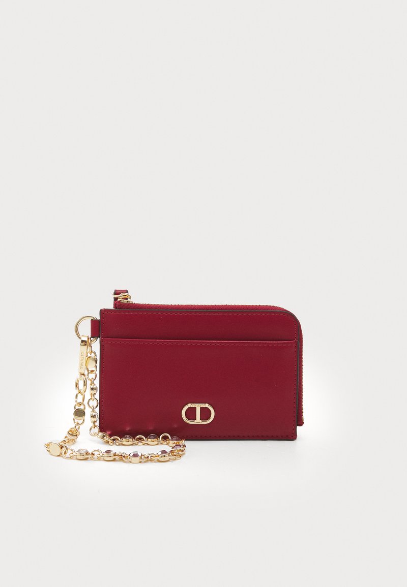 Portafoglio bordeaux realizzato in pelle liscia con una tracolla in catena dorata, dotato di chiusura con zip e un logo decorativo sul fronte.