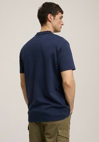 Granatowa koszulka z krótkim rękawem w gładkiej bawełnianej mieszance o klasycznym kroju. Czysta linia dekoltu i prosty design, noszona z beżowymi spodniami cargo.