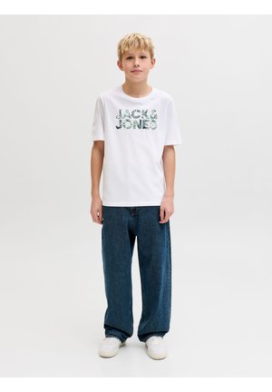 Blond boy standing, wearing a white Jack & Jones t-shirt, loose blue jeans, and white sneakers against a plain white background.