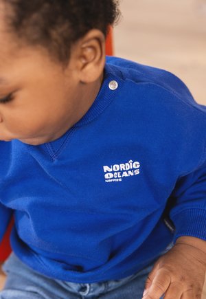 Blauwe sweater met een zachte textuur, voorzien van een logo "NORDIC OCEANS" in het wit. De hals heeft een drukknoopdetail.