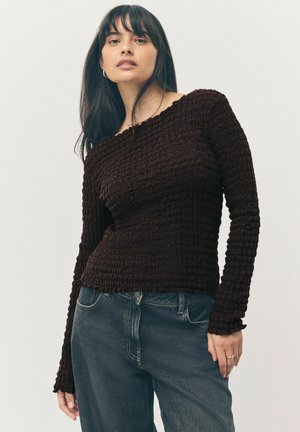 Bruine textuur lange mouw top met een geribbeld ontwerp, voorzien van een off-shoulder halslijn en een aansluitende silhouet, gecombineerd met donkere denim jeans.