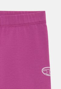 Vijolične legice iz raztegljive tkanine z gladko teksturo, ki imajo elastičen pas in majhen bel logotip blizu roba.