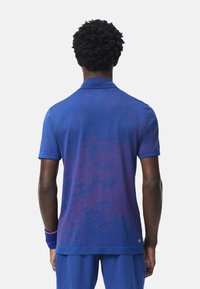 Blå polo skjorta med en gradient och ett texturerat mönster; korta ärmar, krage, och en etikett vid fållen med "DRY"-märke.