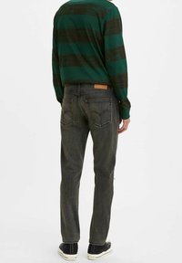 Camisa de manga larga verde y negra a rayas con cuello redondo, combinada con jeans ajustados gris oscuro y zapatillas negras con suelas blancas.