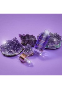 Bottiglia di siero in cristallo viola con dettagli in oro rosa, circondata da cristalli di ametista su uno sfondo viola. Inclusa una pipetta trasparente.