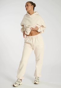 Beige hooded sweatshirt with a relaxed fit and dropped shoulders, paired with matching sweatpants featuring an elastic waistband and logo detail.