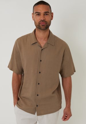 Camisa de manga corta, con botones, en un tejido marrón claro. Presenta un cuello, una textura sutil y botones negros en el frente.