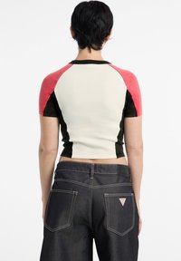 Short-sleeve cropped shirt with red, black, and cream color block design; paired with dark denim jeans featuring back pockets and logo patch.