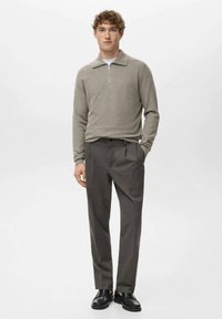 Svetlo siva pulover s četrtinskim zadrgo, v kombinaciji s temno sivo hlačami in črnimi čevlji, prikazan na nevtralni ozadju.