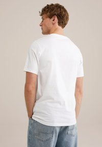 Camiseta blanca de algodón con escote redondo, mangas cortas y diseño liso, combinada con jeans de mezclilla azul claro.