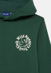 Temno zeleno kapuco z bež grafiko tekače račke, obdano z besedami "Wild Runners Trail Club" na prsih.