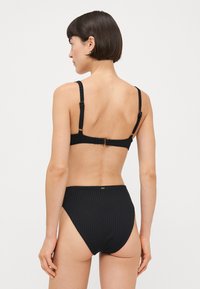 Čierny bikini s rebrovým textúrou. Nastaviteľné ramienka a zapínanie na háčik na zadnej strane. Vysoké nohavičky s čistým, minimalistickým dizajnom.