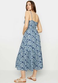 Abito maxi floreale in blu chiaro con motivi blu scuro, spalline sottili regolabili, schiena elastica e gonna a balze. Sandali piatti visibili.