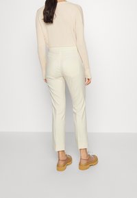 Pantalon ajusté de couleur claire, taille haute avec jambes droites, associé à un pull à manches longues et des sabots à semelles épaisses. Texture lisse.