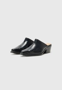 Mules de couro preto com bico fino, detalhe de costura em onda discreta e um salto bloco médio. Textura suave e design elegante.