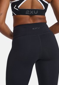 Schwarze, hoch taillierte Leggings mit glatter Textur und verstärkten Nähten, die ein dezentes Logo am Bund und kontrastierende Nähte aufweisen.