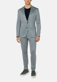 Lichtgrijs pak van textiel met structuur, met een enkelboeks jasje met twee voorzakken, gecombineerd met bijpassende slim-fit broek en sneakers.