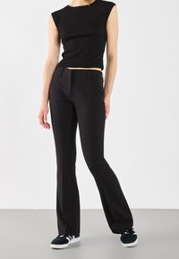 Black fitted sleeveless top paired with black flared trousers. Both garments have a smooth texture, creating a sleek, monochromatic look.