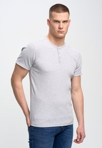 Camisa henley de manga corta gris con cuello de tres botones, tejido texturizado, diseño ajustado, combinada con vaqueros azules.