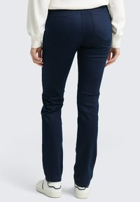 Marineblaue, taillierte Hose mit einer glatten Textur, verfügt über zwei Gesäßtaschen und ein dezentes Bootcut-Design, getragen mit weißen Sneakers.