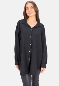 Black button-up shirt made of textured fabric with a collared neck, long sleeves, and a slightly oversized fit. Features silver buttons.