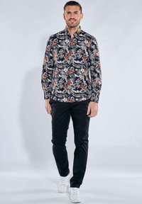 Schwarzes Langarmhemd mit buntem Blumenmuster, kombiniert mit schwarzen Hosen und weißen Sneakern. Glattes Material und klassisches Kragen Design.