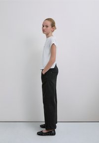 Tricou alb cu mâneci scurte, combinat cu pantaloni negri cu picioare largi, prevăzuți cu buzunare laterale și balerini negri cu nituri, pe un fundal simplu.