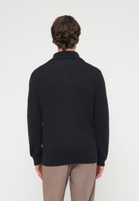 Πλεκτό πουλόβερ σε ναυτικό μπλε με ριγωτή υφή, ψηλό γιακά και μακριά μανίκια, σχεδιασμένο για χαλαρή εφαρμογή και διακριτική απαλή υφή.